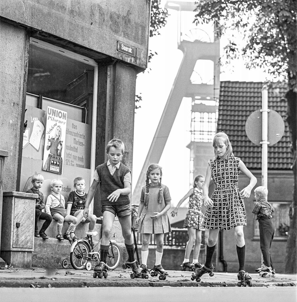 Spielende Kinder auf Rollschuhen, im Hintergrund der Förderturm von Zeche Mont Cenis in Herne-Sodingen, um 1970. Foto: LWL/Orwat